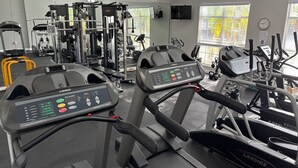 Une salle de sport équipée de tapis de course, d’appareils de musculation et d’un miroir.