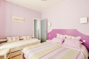 A bedroom with two beds, a desk, and a door leading to another room.