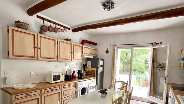 A kitchen with wooden cabinets, a dining table with chairs, a microwave, and a refrigerator. - Provençal farmhouse in the countryside, with air conditioning and a pool, near Avignon (Monteux)