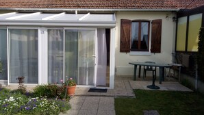 A house with a sliding glass door, a small patio with a table and chairs, and a garden with various plants. - Charming south facing house completely renovated with garden (Dives-sur-Mer)