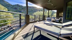 A balcony with a view of a mountainous landscape, a ceiling fan, and a seating area with a table and chairs.