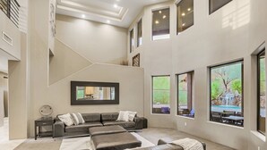 A spacious living room with a large sectional sofa, a fireplace, and multiple windows offering views of a landscaped outdoor area.