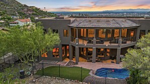 A modern multi-story house with a rooftop patio, a swimming pool, and a view of the surrounding landscape.