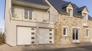 A two-story house with a garage, a balcony with a metal railing, and a stone facade. - Independent house facing the sea with balcony and terrace (Saint-Vaast-la-Hougue)
