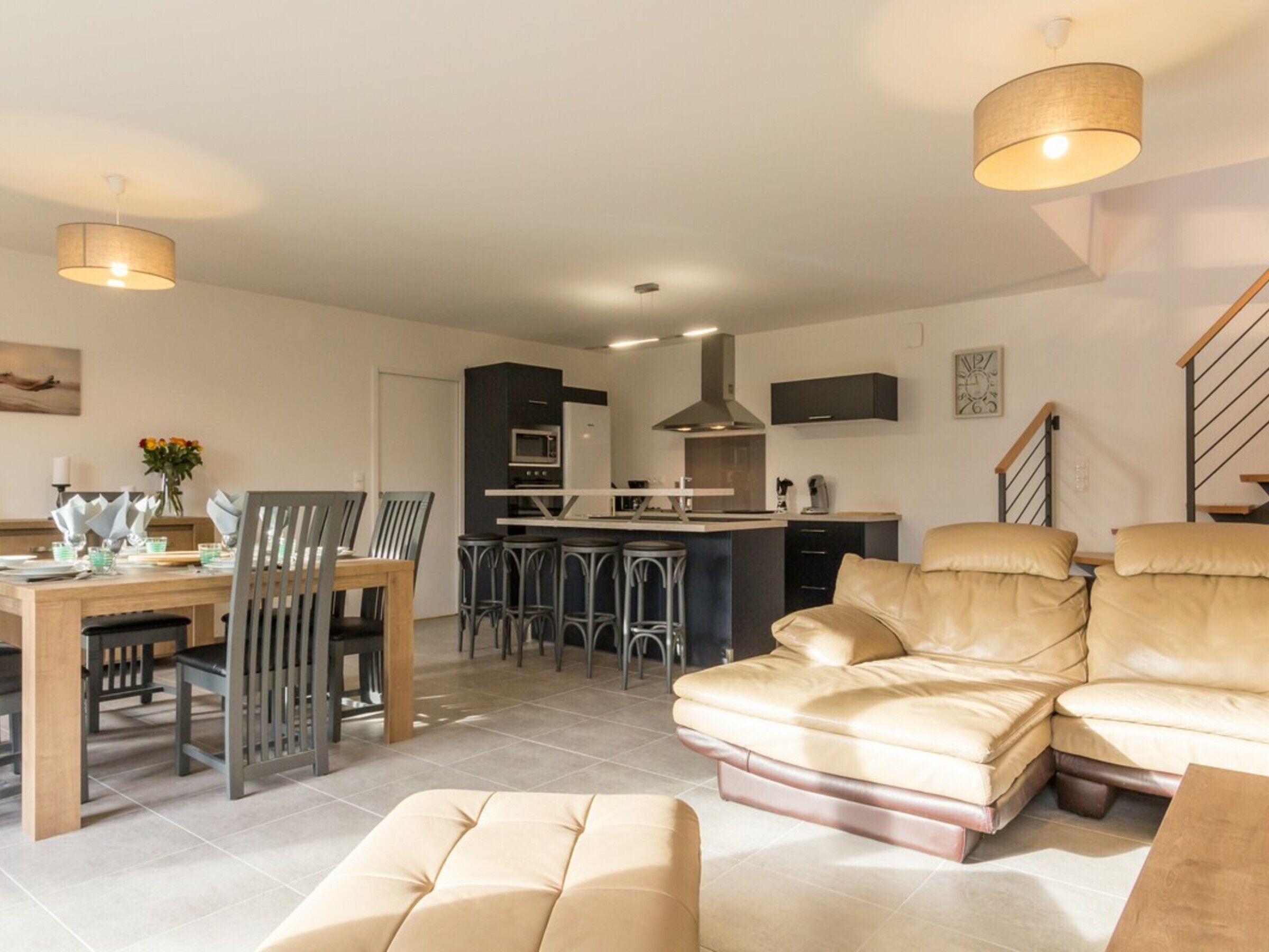 Un salon moderne comprenant un canapé, un pouf et un coin repas avec des chaises et une table.