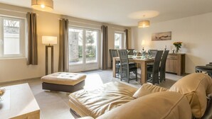A spacious living room with a large window, a dining area, and a kitchen in the background. - Independent house facing the sea with balcony and terrace (Saint-Vaast-la-Hougue)