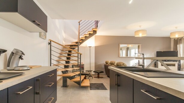 A modern kitchen with a central island, dark cabinetry, and a wooden staircase. - Independent house facing the sea with balcony and terrace (Saint-Vaast-la-Hougue)