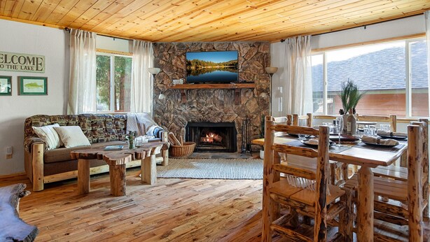 A cozy lodge interior with a stone fireplace, wooden furniture, and a large window overlooking a lake.