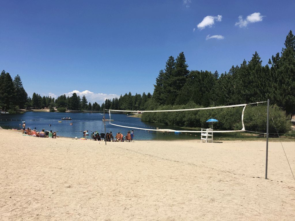 A beach volleyball court with a net, surrounded by sand and a lake.