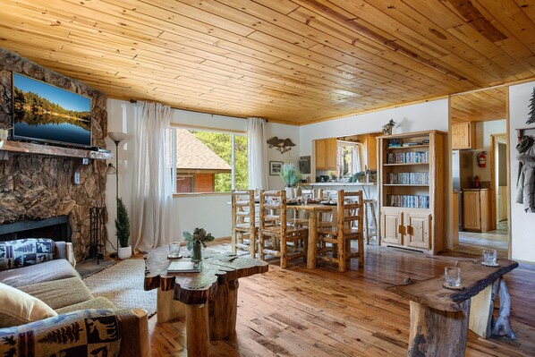 Een gezellig blokhutinterieur met een stenen open haard, een houten eettafel en een keukenhoek.