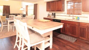 Ein Essbereich mit Holztisch und -stühlen, eine Küche mit Holzausstattung und Spüle sowie ein Fenster mit Jalousien.