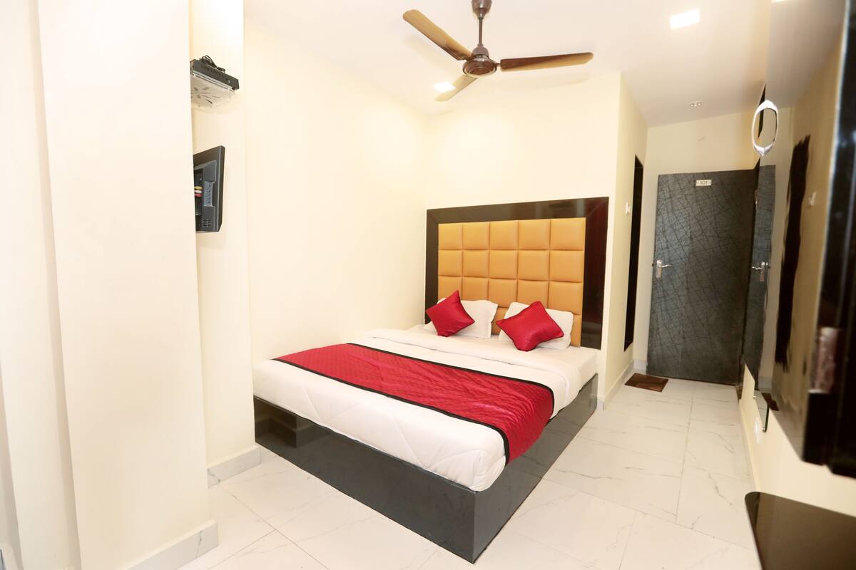 A hotel room with a bed, a ceiling fan, a TV, and a door.