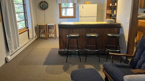 A cozy kitchen with a bar area, wooden stools, a refrigerator, and a window with curtains. - 
 Enjoy Our Cabin And Sunsets, On Peaceful , Non-Motorized  Lulu Lake (Shawano)