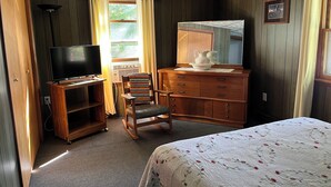A bedroom with a bed, a desk with a television, a chair, a dresser, and a window with curtains. - 
 Enjoy Our Cabin And Sunsets, On Peaceful , Non-Motorized  Lulu Lake (Shawano)