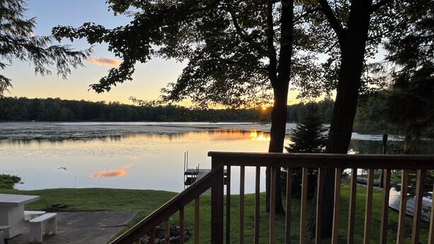 A wooden deck with a railing overlooking a calm lake at sunset. - 
 Enjoy Our Cabin And Sunsets, On Peaceful , Non-Motorized  Lulu Lake (Shawano)