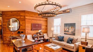 A cozy living room with a wooden wall, a chandelier, a sofa, a coffee table, and a bookshelf. - Spacious, Private 3BR Suite: Steps to King (Charleston)