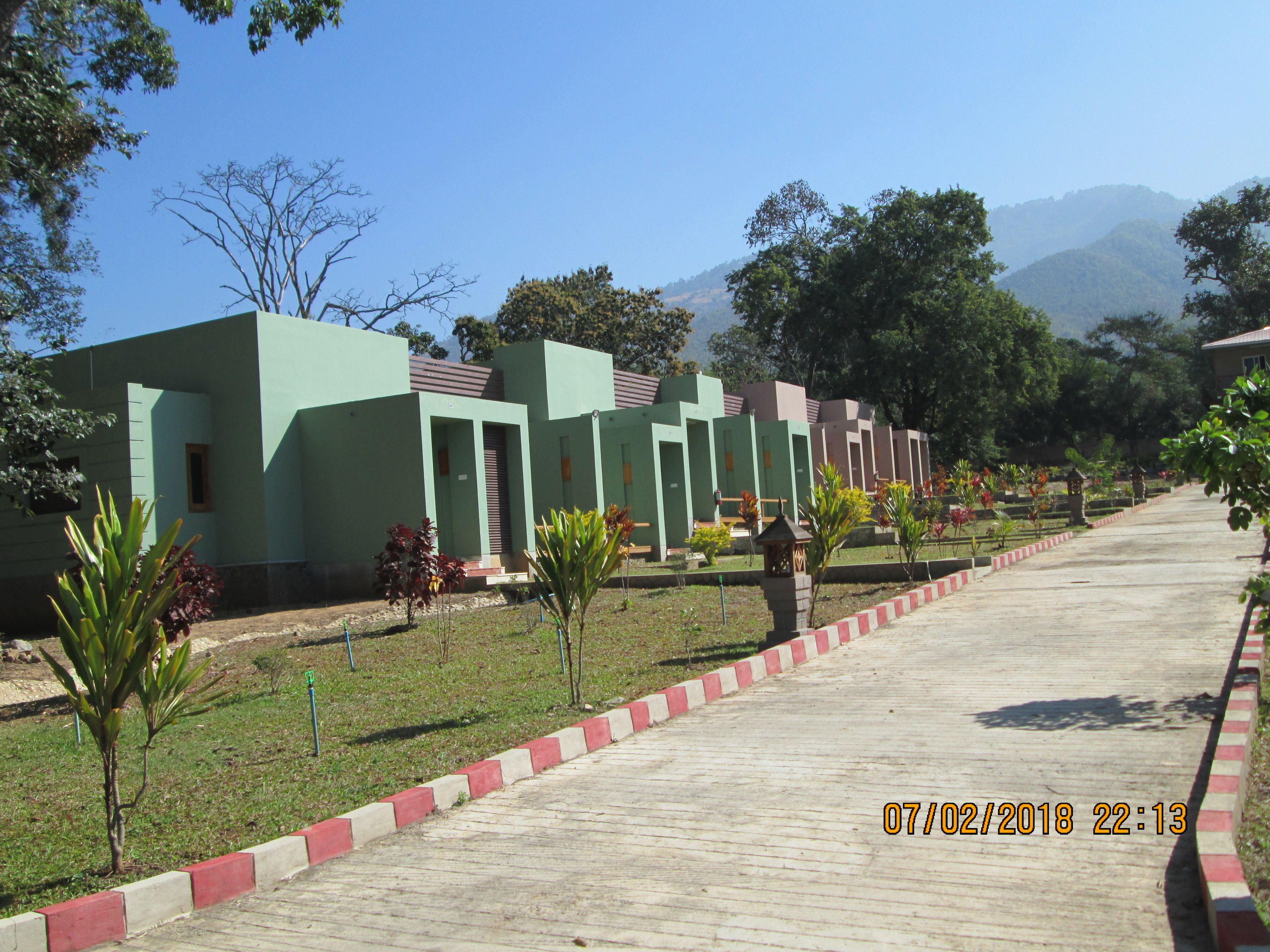 A row of green buildings with a paved walkway and small plants.