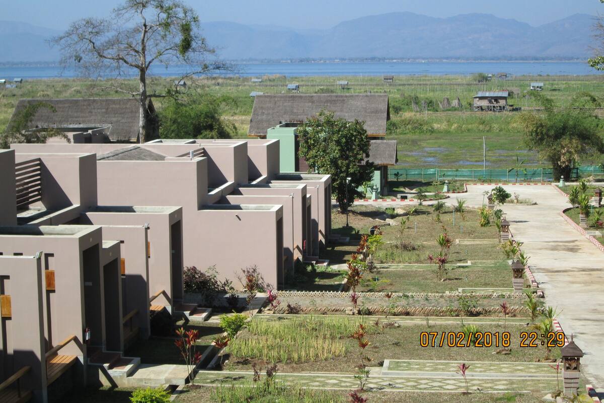 Ein Wohngebiet mit modernen Gebäuden, einem gepflegten Garten und Blick auf das Meer und die Berge im Hintergrund.