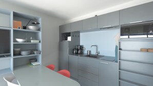 A modern kitchen with grey cabinets, a white countertop, and a built-in oven. There are two red chairs and a white table. - Seaside Apartment with Balcony, Close to Shops (Les Sables-d'Olonne)