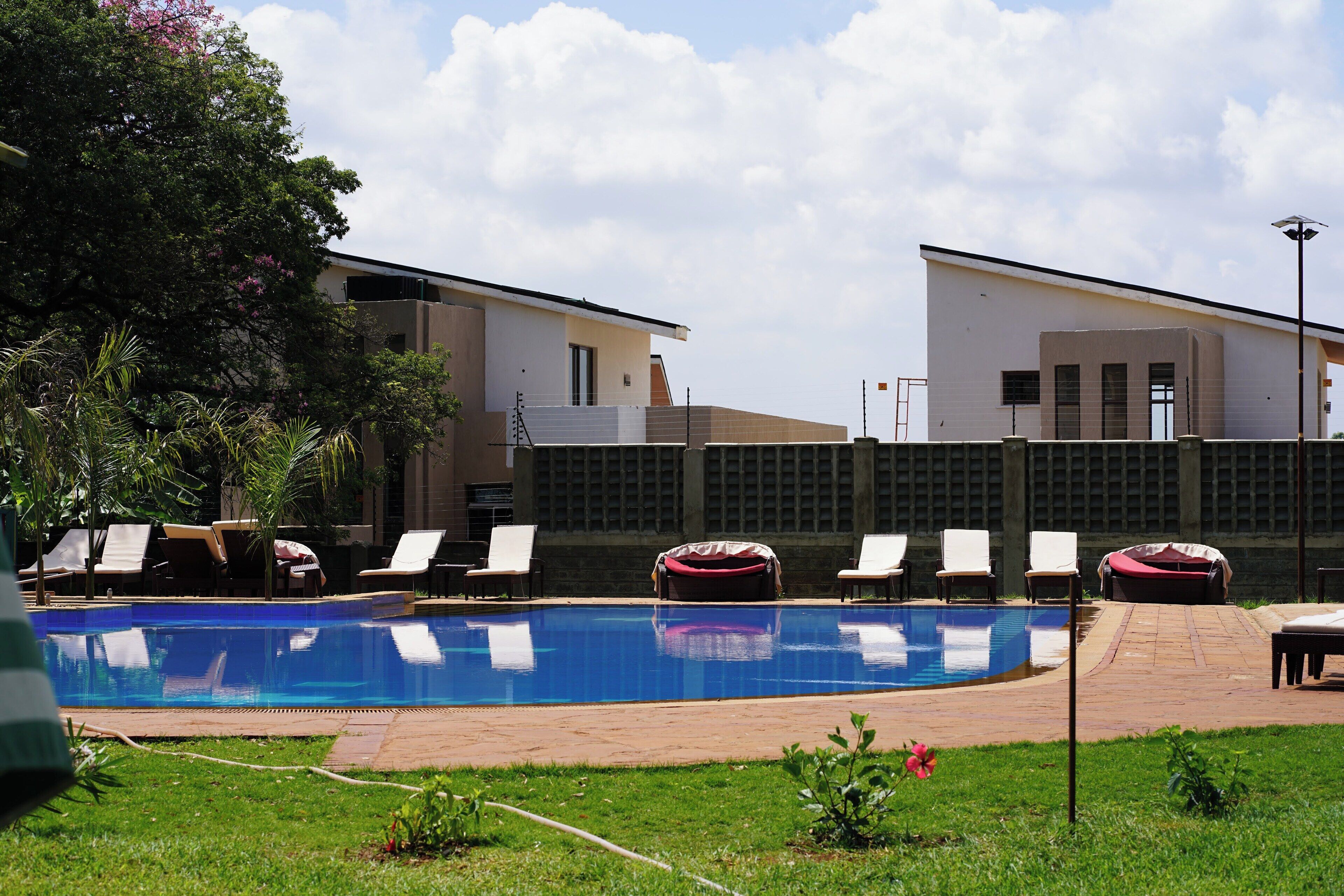 A swimming pool with lounge chairs, a covered seating area, and a building with a tiled exterior.