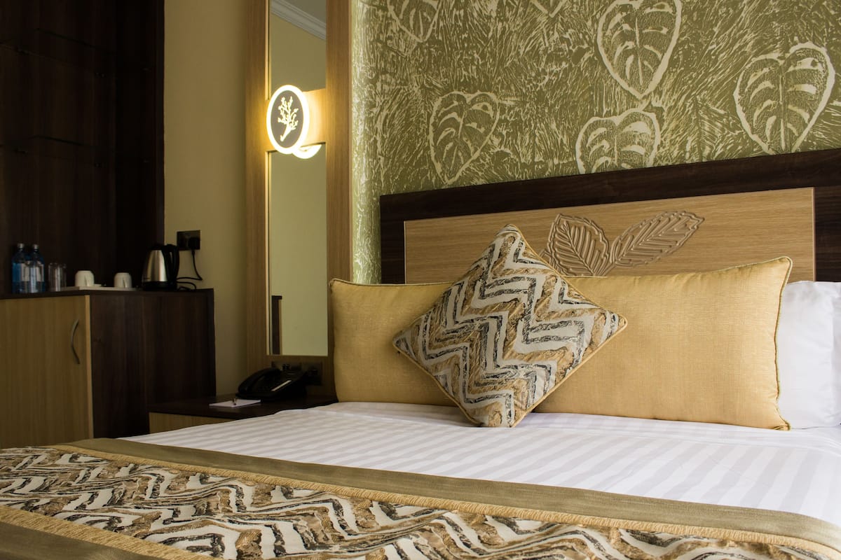 Quarto de hotel com cama, mesa de cabeceira, abajur e espelho.