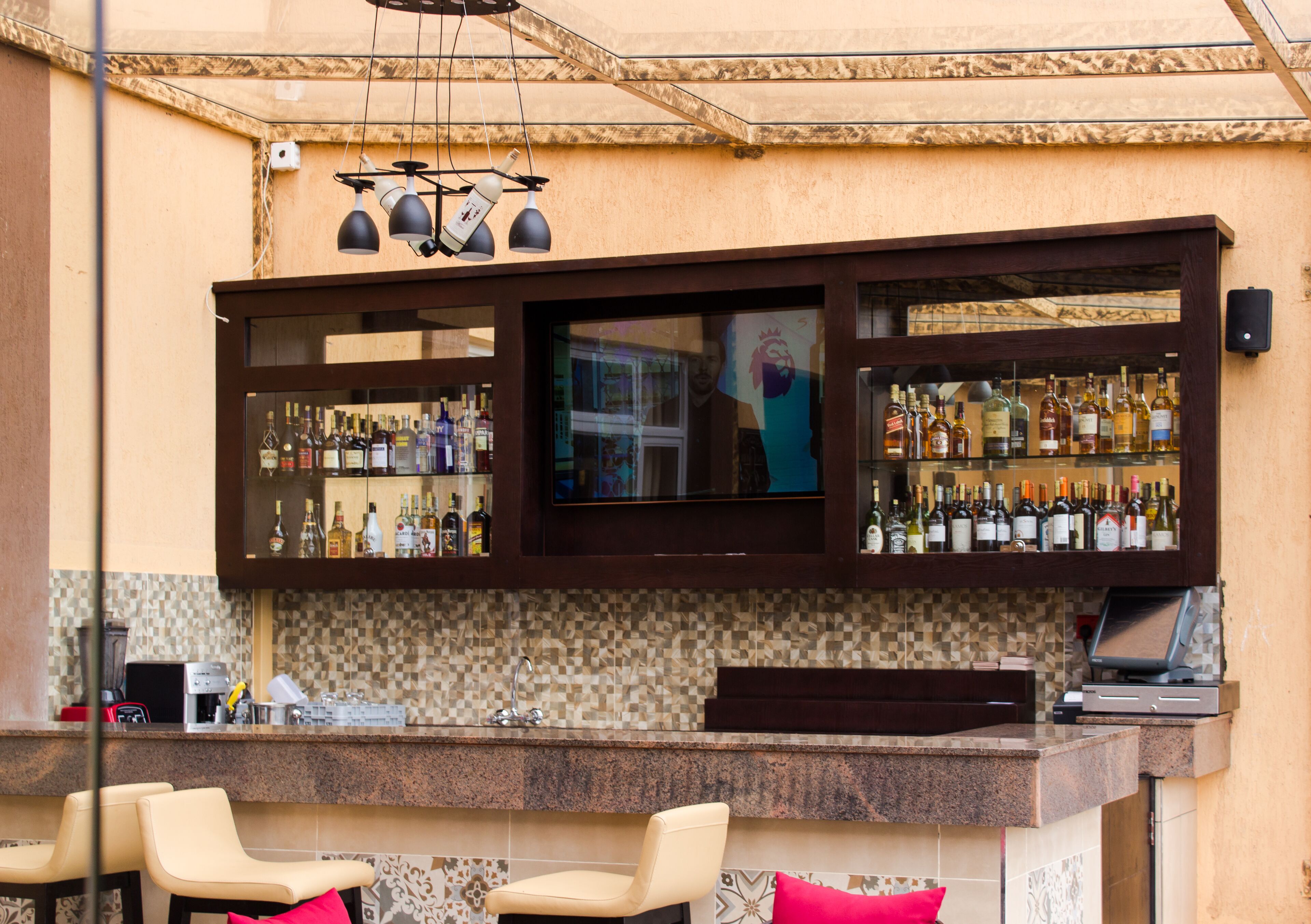 Zona de bar con mostrador, diversas opciones de asientos, televisor y una variedad de botellas.