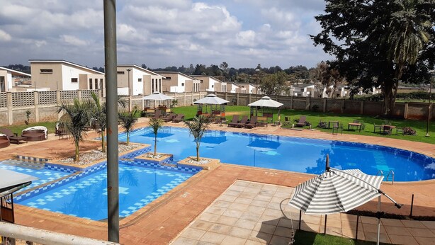 A swimming pool with lounge chairs and umbrellas, surrounded by a brick patio and a grassy area with trees. - Elysian Resort (Nairobi)