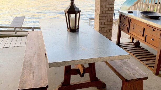 Una mesa de madera con bancos y un farol sobre una terraza de concreto con vista al agua.