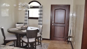 Un'area pranzo con un tavolo rotondo, quattro sedie, un lampadario, una finestra con tende e una porta in legno.