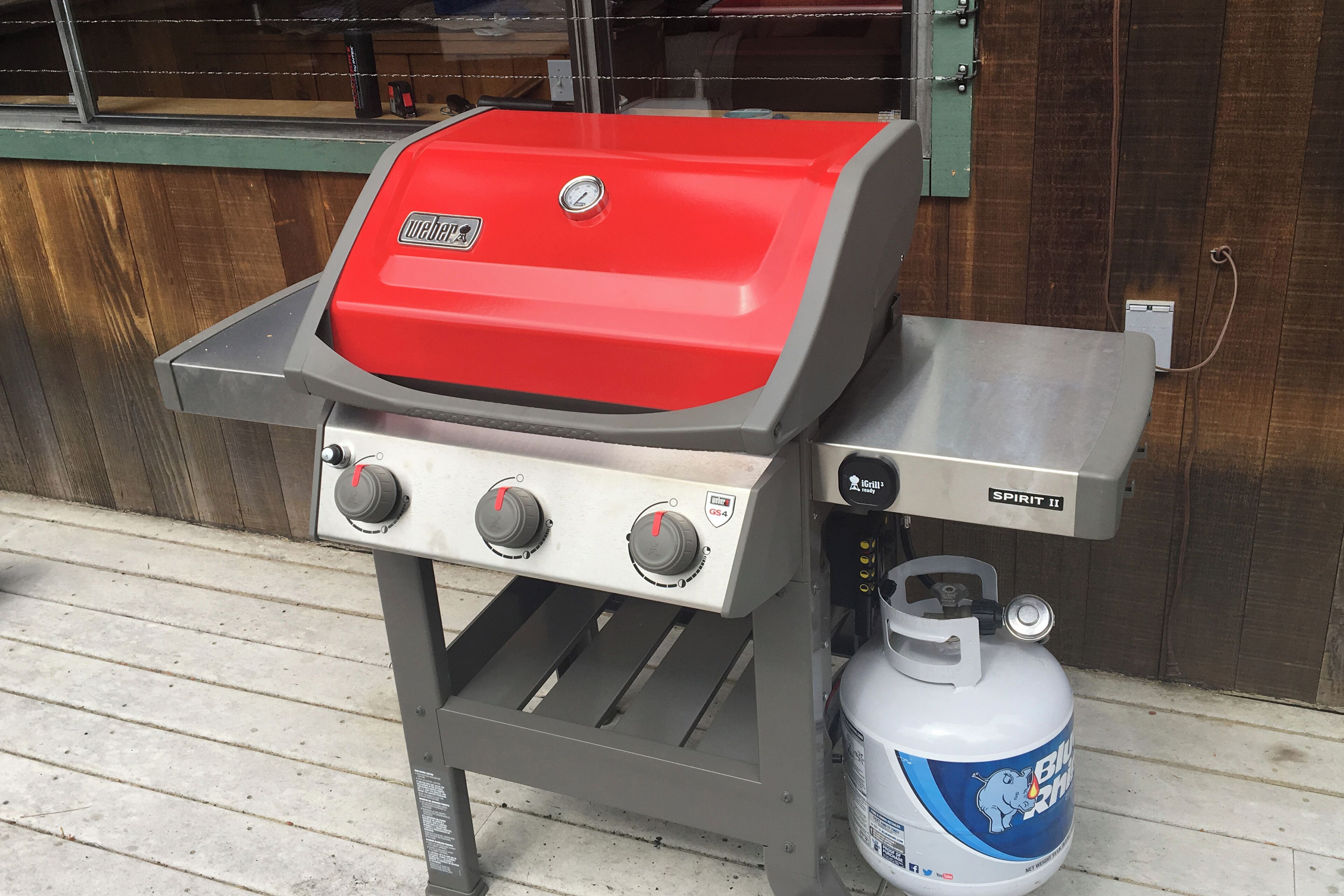En portabel gasolgrill med ett rött lock och tre justeringsknappar, en gasolflaska och ett grillstativ i metall.