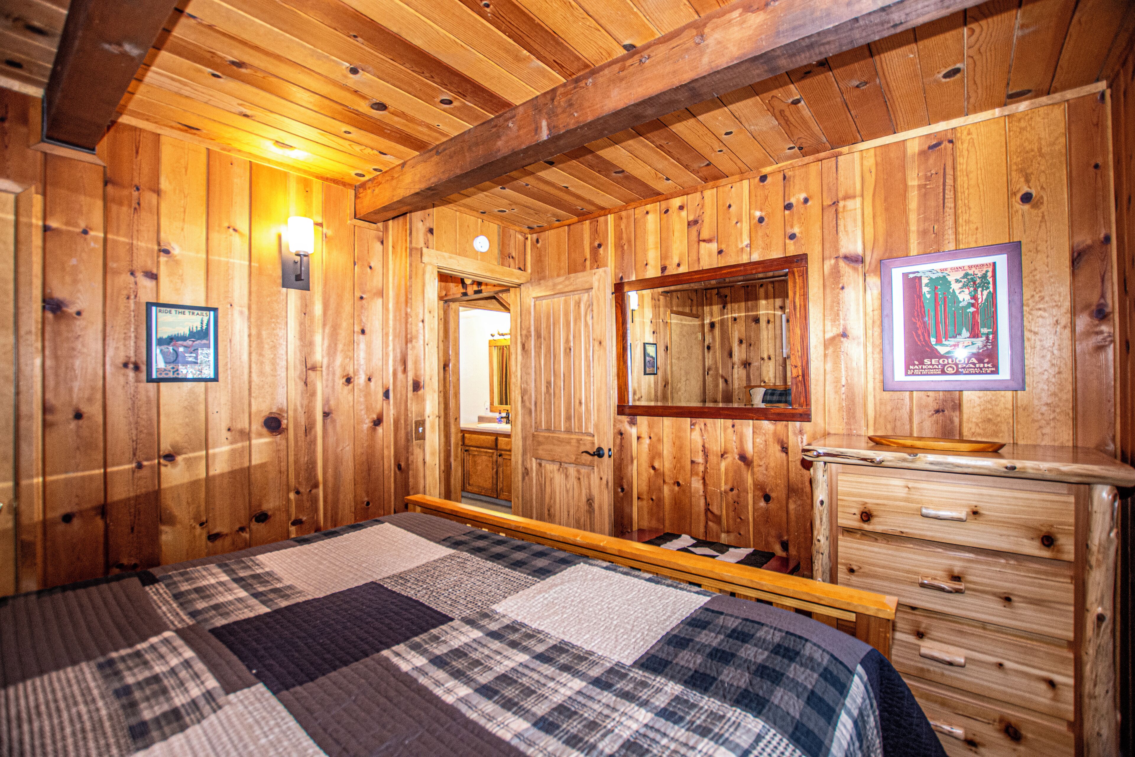 Un dormitorio de cabaña de madera con cama, cómoda, espejo y lámpara de pared.