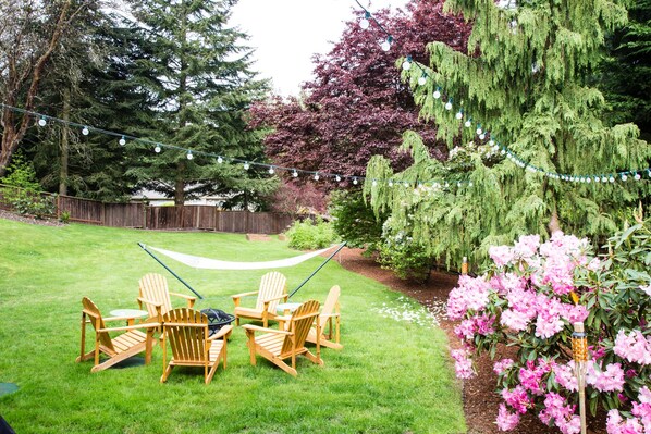 Relax in a serene backyard oasis with a seating area, hammock, and lush greenery.