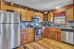 Enjoy meals with a view from this kitchen, which features a refrigerator, oven, and cabinets, plus a window overlooking the outdoors.