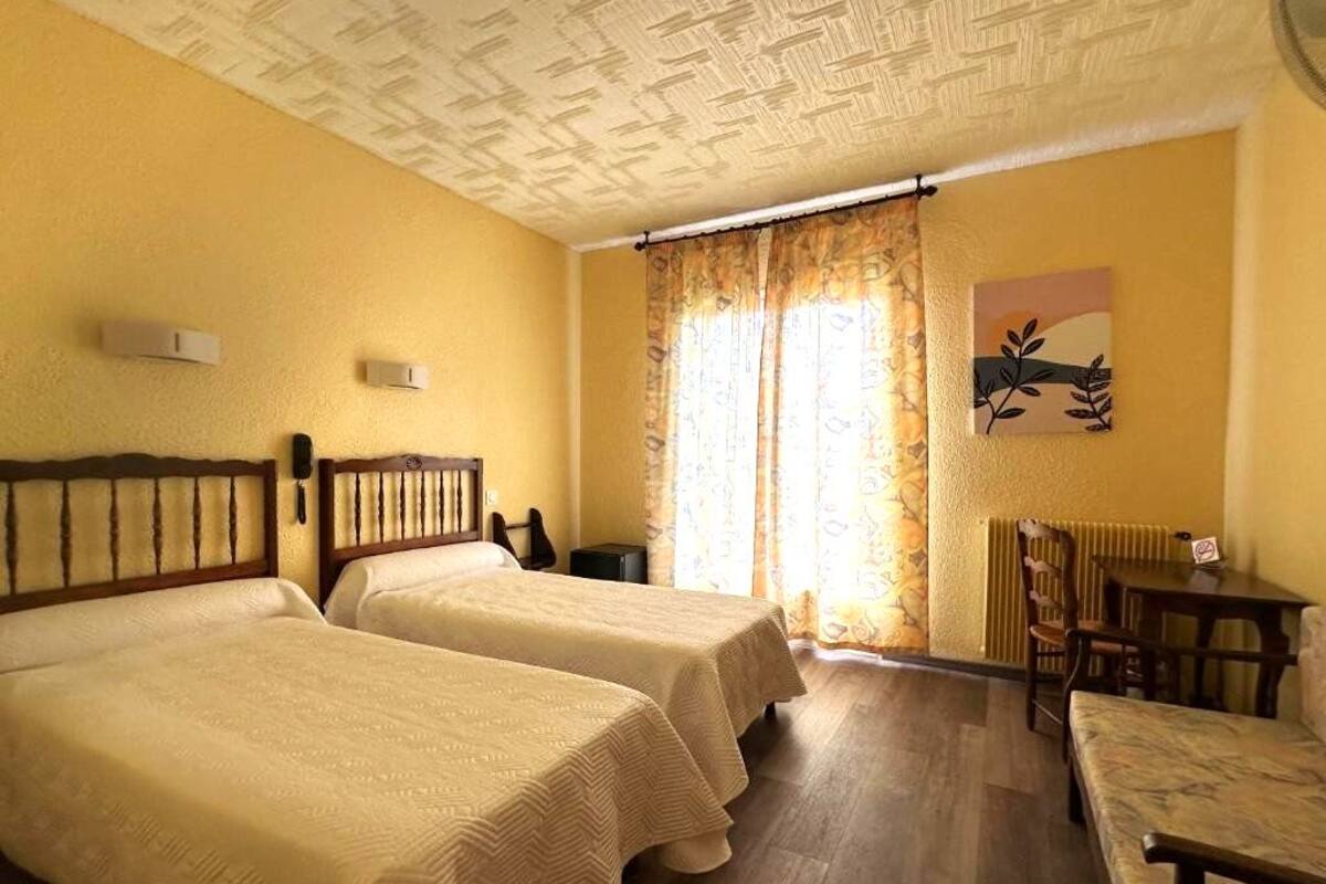 A hotel room with two beds, a wooden headboard, a desk with a chair, and a radiator.