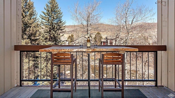Een balkon met een houten tafel en twee stoelen, met uitzicht op een bergachtig landschap.