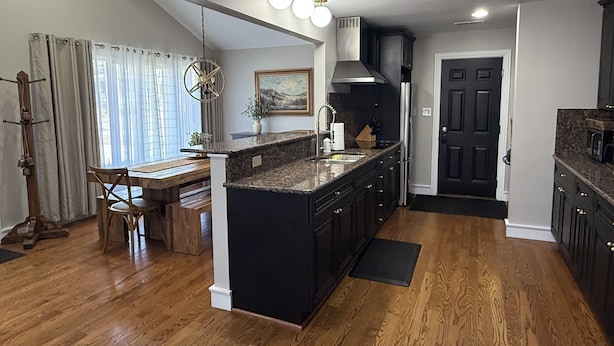 A modern kitchen with dark cabinetry, a central island, and a dining area with a wooden bench and table.
