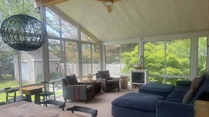 A sunroom with large windows, a wooden table, two sofas, and a television.