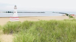 A lighthouse on a sandy beach with a grassy foreground and a calm sea in the background.