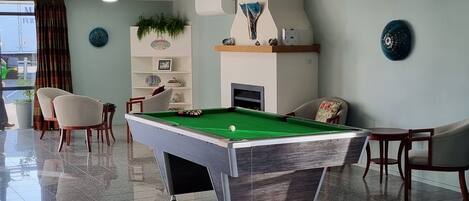 Une table de billard dans une pièce bien éclairée, avec une cheminée, un coin salon et des objets décoratifs.