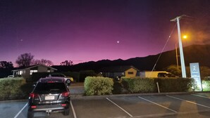 A parking lot with a car, a building with a sign, and a mountain in the background. - Kaikoura Quality Suites (Kaikoura)