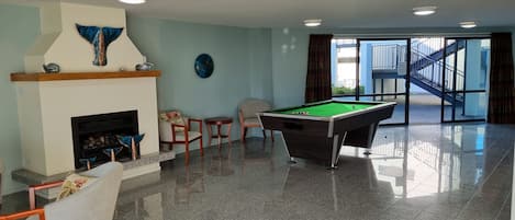 A pool table in a room with a fireplace, chairs, and a view of a building outside.