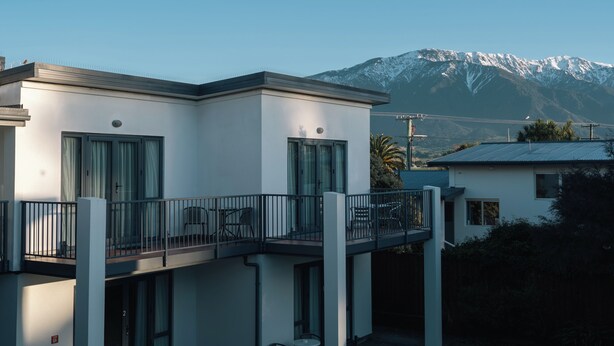 A modern two-story building with a balcony, large windows, and a view of snow-capped mountains. - Kaikoura Quality Suites (Kaikoura)