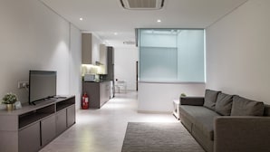 Een moderne woonkamer met een flatscreen televisie, een grijze bank en een groot raam.