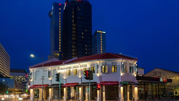 Een hotel met een rood-wit gevel, diverse winkelpanden en een opvallend gebouw op de achtergrond.