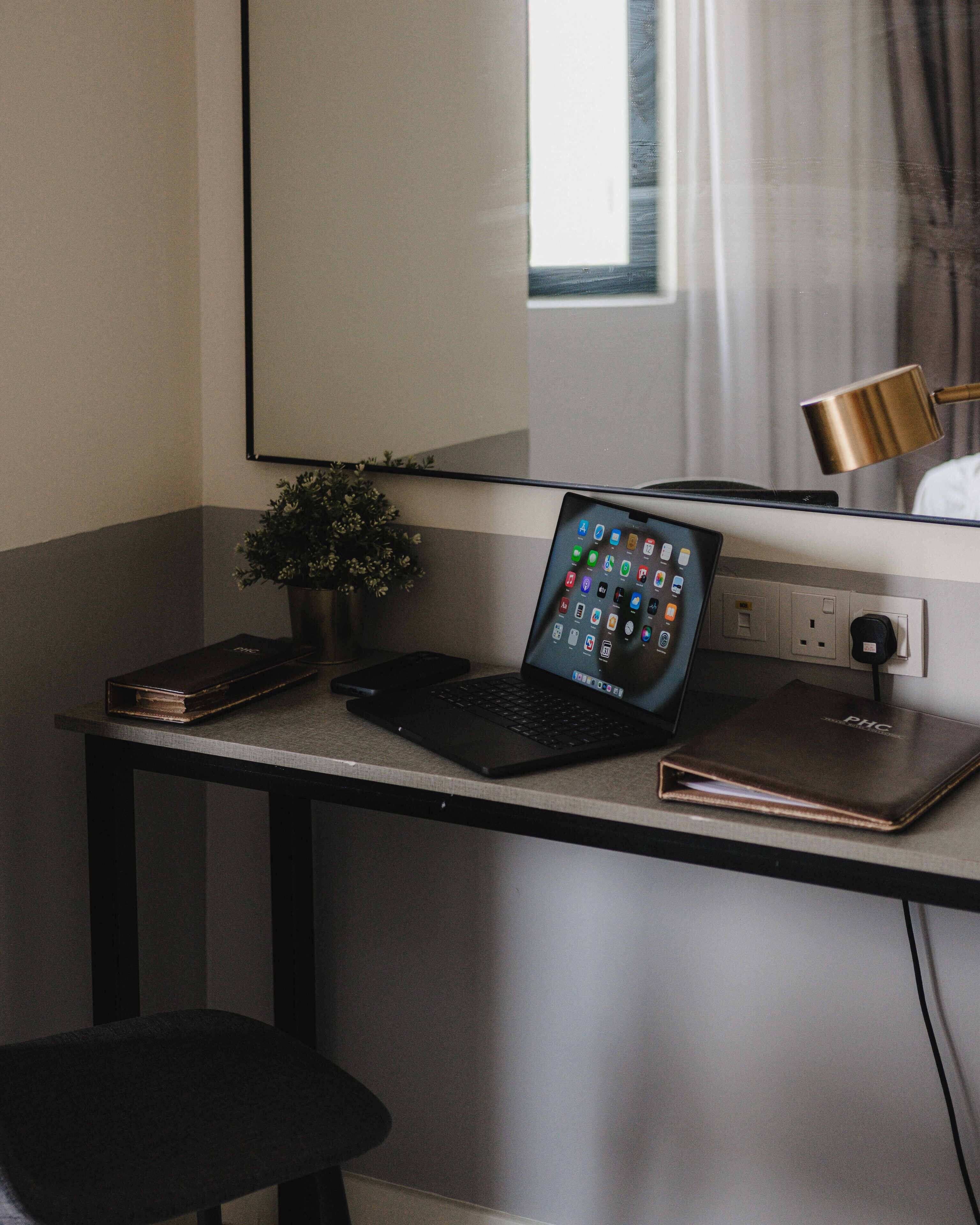 Un bureau avec un ordinateur portable, un téléphone intelligent, un livre, une plante et une lampe.