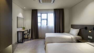 A hotel room with two beds, a desk with a chair, a mirror, and a window with curtains.