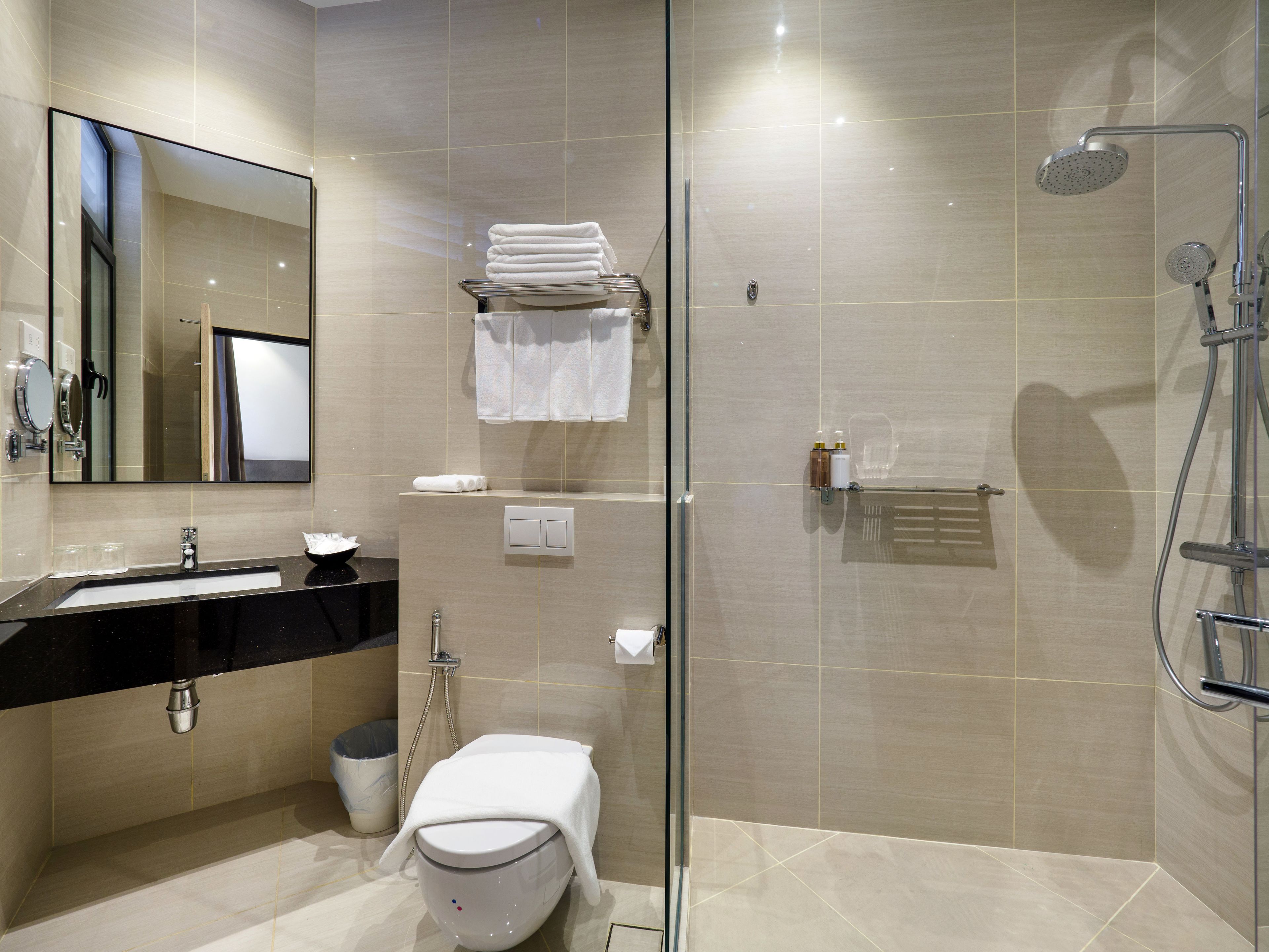 A modern bathroom with a glass-enclosed shower, a sink with a black countertop, and a toilet with a towel on top.