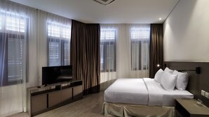 Een moderne hotelkamer met een groot bed, een televisie op een houten dressoir en ramen met gordijnen.