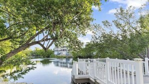 A waterfront property with a white deck, a large tree, and a building in the background. - Casa Largo (Key Largo)