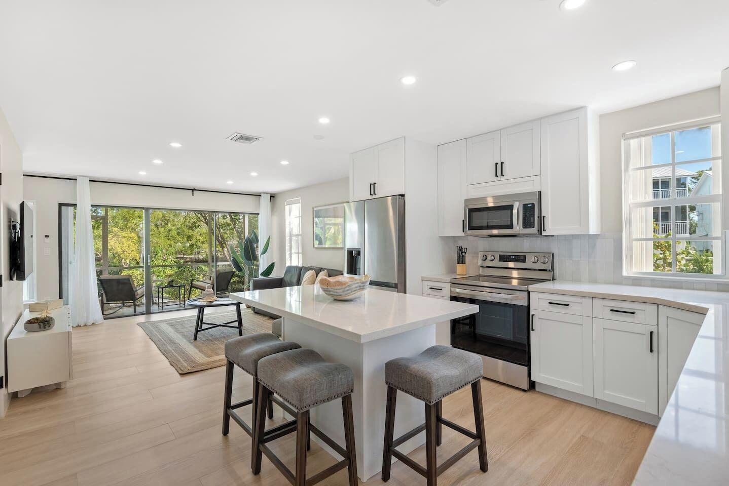 A modern kitchen with white cabinetry, a central island with stools, a dining area with a view, and a large sliding glass door.